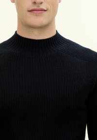 Knitad marinblå polotröja med ribbad textur. Har en figursydd design och upphöjda sömmar vid axlarna för extra detaljer.