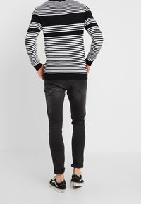Mustikka ja valkoinen raidallinen neulepusero, pyöreä kaula-aukko, pitkät hihat, mustat ribbauskuminauhat hihansuissa ja helma, yhdistetty mustien slim fit -farkkujen ja mustien lenkkareiden kanssa.