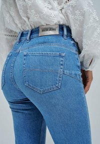 Vaqueros de mezclilla azul de talle alto, corte recto, con una etiqueta de cuero "SALSA JEANS" y dos bolsillos traseros con costuras visibles.