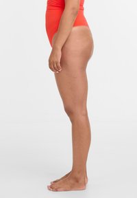 Roter Einteiler-Badeanzug mit hohem Beinausschnitt. Glatter, elastischer Stoff, minimale Abdeckung an den Seiten und keine sichtbaren Verschlüsse.