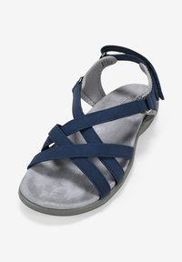 Sandal color blu navy con cinturini incrociati, parte superiore morbida simile al camoscio e suola interna grigia imbottita. Presenta una cinghia alla caviglia con fibbia regolabile.
