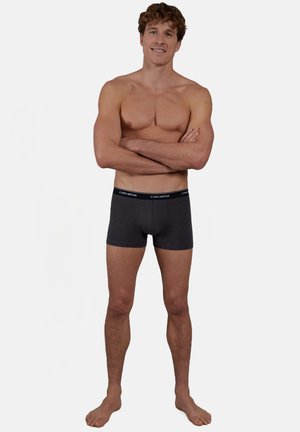 Graue Boxershorts aus Baumwolle mit einem schwarzen elastischen Bund, der das Logo "ceetba" in Weiß zeigt. Das Modell steht mit verschränkten Armen.