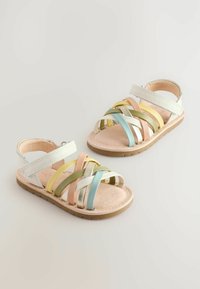 Sandalias con tira featuring bandas en colores pastel de rosa, amarillo, verde, azul y toques metálicos. Suela plana y flexible con una tira en la parte posterior.