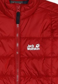 Veste isolante rouge avec un design matelassé, fermeture éclair intégrale et accents noirs. Présente le logo blanc de Jack Wolfskin à l'avant.