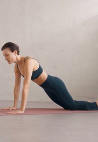 Czarny sportowy top i legginsy, pozująca w pozycji deski na macie do jogi, gładka faktura, minimalistyczny design, neutralne tło.