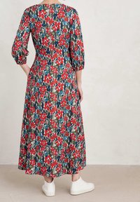 Robe maxi fleurie avec des motifs rouges et bleus sur fond sombre, dotée de manches bouffantes 3/4 et d'une coupe décontractée. Associée à des chaussures blanches.