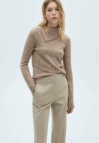 Pull en tricot beige texturé avec un large col replié, associé à un pantalon taillé beige clair avec des poches latérales.