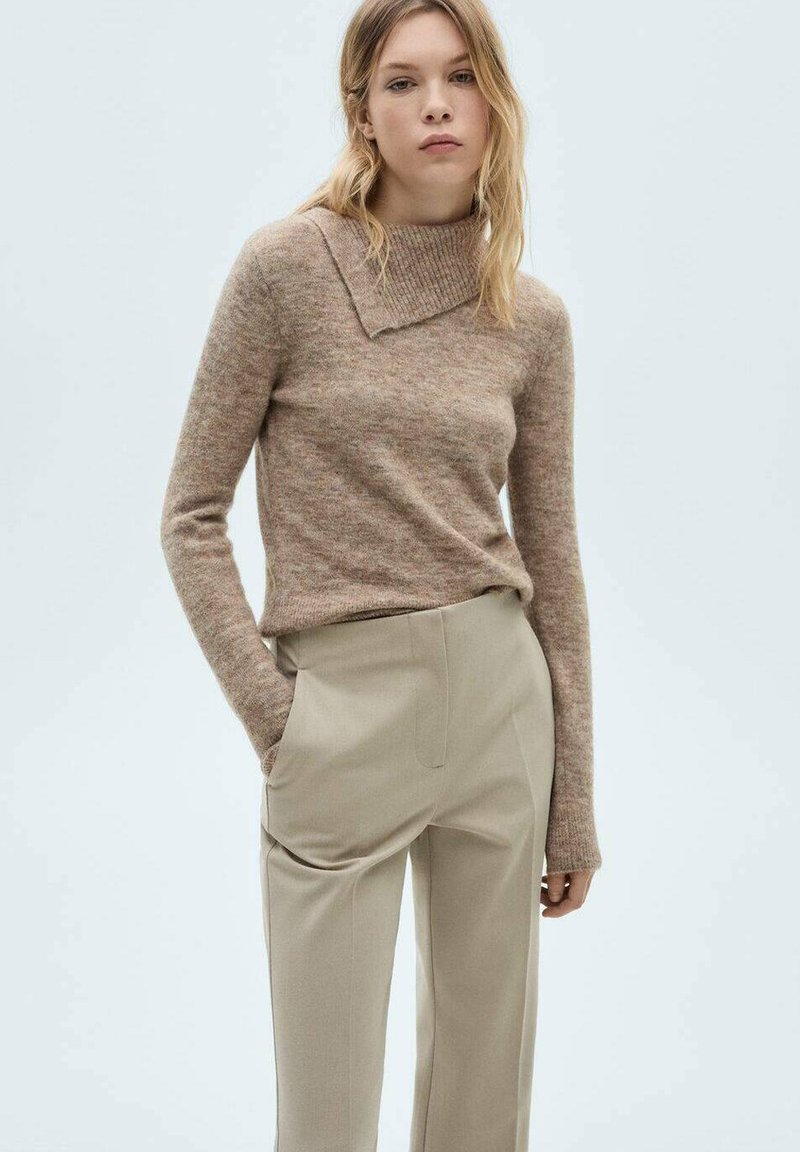 Pull en tricot beige texturé avec un large col replié, associé à un pantalon taillé beige clair avec des poches latérales.