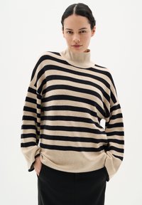 Pulover tricotat în dungi, bej și negru, cu guler înalt, croi lejer și mâneci lungi cu mansetă pliată. Textură moale și design casual.