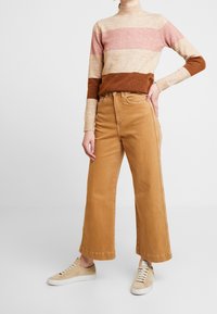 Beige- och bruna randiga stickade tröjor med hög krage, kombinerad med vida tanbyxor och ljusbruna sneakers.