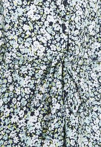 Abito floreale con motivo nero, bianco e verde, chiusura frontale a bottoni, vita arricciata e texture di tessuto morbido.