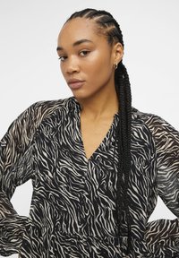Blusa con motivo zebra nera e beige, con scollatura a V, maniche lunghe trasparenti e corpino aderente, realizzata in tessuto testurizzato e con orlo a strati.