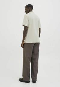Camiseta polo en beige claro, fabricada con un tejido texturizado, de manga corta; combinada con pantalones sueltos de corte amplio en marrón oscuro, con bolsillos y dobladillos acampanados.