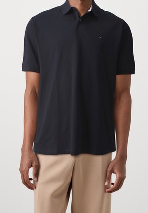 Mørkeblå polo med korteærmer i bomuld, med klassisk krave og diskret logodetalje på venstre bryst. Kombineret med lyse beige bukser.