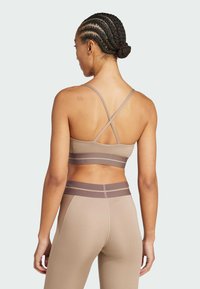 Set od bralettea i tajica u svijetlosmeđoj boji. Bralette ima povezane naramenice, a tajice imaju kontrastni smeđi pojas i bočne pruge.