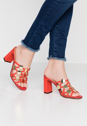 Červené sandály na vysokém podpatku s křížovými pásky zdobenými zlatými kulatými akcenty; texturovaný materiál se silným blokovým podpatkem.