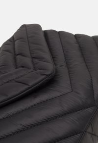 Černá prošívaná péřová bunda s prošitým vzorem. Má sklopený límec a viditelné švy ve vzoru rybí kosti. Hladká, lesklá látka.