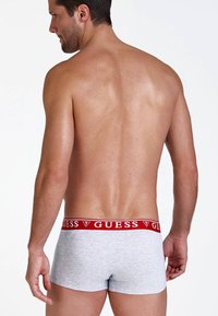 Boxeri din bumbac gri, cu un brâu roșu, având logo-ul "GUESS" afișat pe partea din spate, cu o textură netedă și un design ajustat.