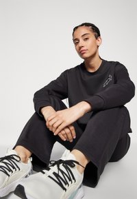 Felpa nera a maniche lunghe con un piccolo design stampato, abbinata a pantaloni jogger neri e sneakers bianche con lacci neri e suole testurizzate.