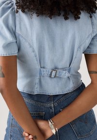 Lichtblauwe denim cropped top met pofmouwen, voorzien van een sluiting aan de achterkant. Gecombineerd met hoge taille blauwe denim jeans.