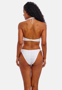 Conjunto de bikini blanco con textura estampada, tirantes al cuello y cierre trasero ajustable. La parte inferior tiene un diseño de corte alto.