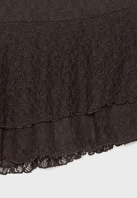 Tissu en dentelle superposée marron foncé avec motifs floraux et bords festonnés sur fond gris.