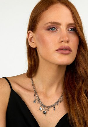 Collana in argento con più ciondoli, caratterizzata da diverse forme e dettagli. Indossata sopra un top nero a spalline sottili.