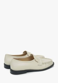 Cream leather loafers with a stitched design, featuring a wide front strap and a textured back. Black rubber sole.