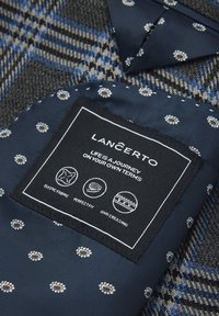 Granatowa etykieta z materiału z białym tekstem i ikonami, podkreślająca elastyczny materiał, idealne dopasowanie i właściwości antygniotące. Wzorzyste tło.