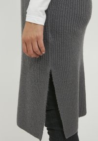 Robe en maille côtelée grise avec fentes sur les côtés ; tissu texturé ; portée sur une chemise blanche à manches longues ; silhouette ajustée ; design minimaliste.