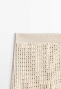 Close-up van beige gebreide stof met verticale gaten en een soepele tailleband.