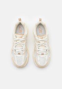 Hvite sportssko med mesh-overdel, beige detaljer og flate lisser. Har en teksturert såle og en løkkefor å lette påkleden.