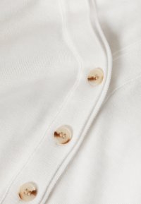 Gros plan sur un tissu blanc en tricot avec trois boutons marbrés beiges cousus le long d'une bordure côtelée.