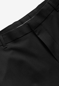 Pantalones negros con un tejido suave y Texturizado, con un frente plano y una cintura estándar con trabillas para cinturón. Detalles de diseño limpios y minimalistas.