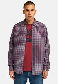 Rood en blauw geruit overhemd met knopen en een kraag, gedragen over een rood graphic t-shirt met een bomenontwerp. Casual fit, lichtgewicht stof.