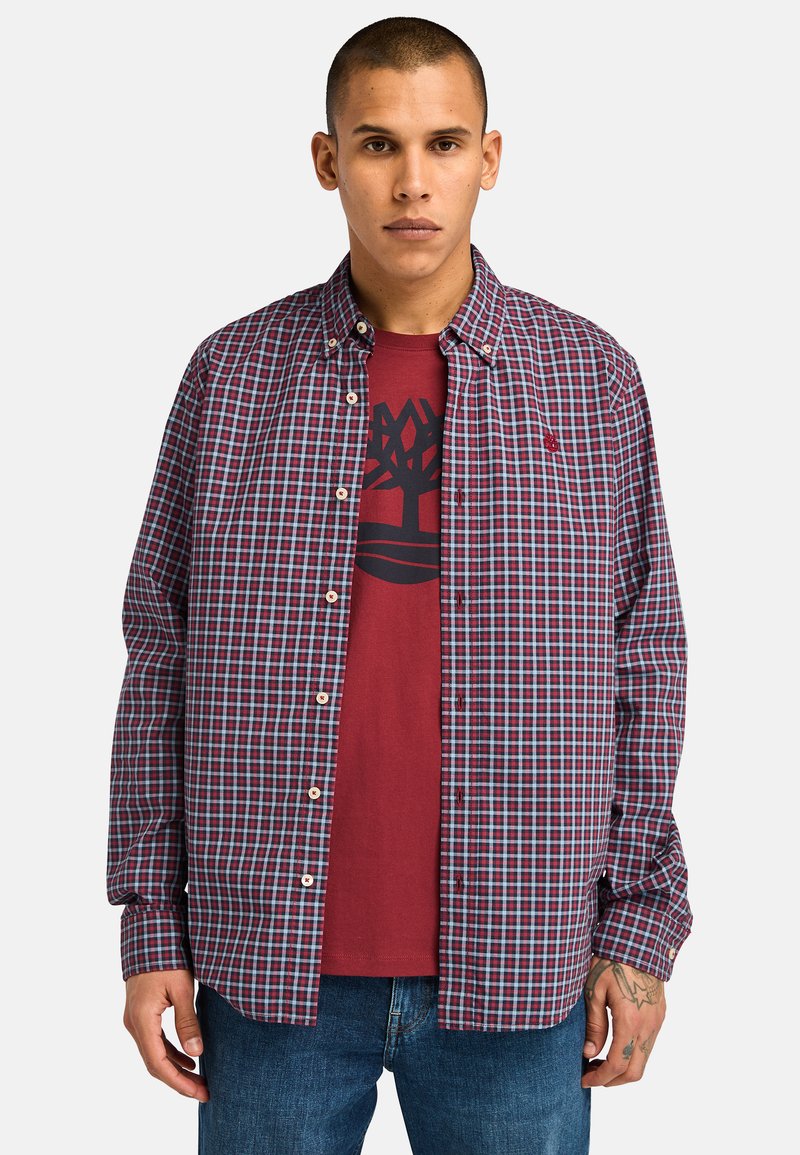 Camicia a quadri rossa e blu con colletto, indossata sopra una t-shirt grafica rossa con un design di un albero. Vestibilità casual, tessuto leggero.