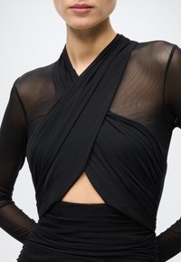 Black top featuring a wrap design with sheer mesh long sleeves and a textured bodice, accented by a central keyhole cutout.