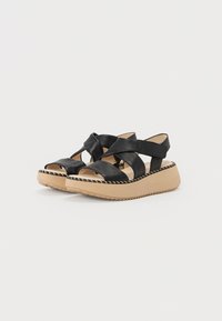 Sorte lær sandaler med kryssede stropper, en plattformsåle med en teksturert beige bunn, og dekorativ søm langs kanten.
