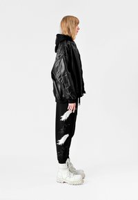Chaqueta bomber de cuero negra sobre una sudadera con capucha negra, combinada con joggers negros con bordados de plumas blancas y botas militares blancas.