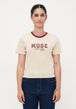 Beige bomull t-skjorte med maroon rund hals og korte ermer. Har "MUSE Energy" grafikk i burgunder og svart. Worn med mørke denimjeans.