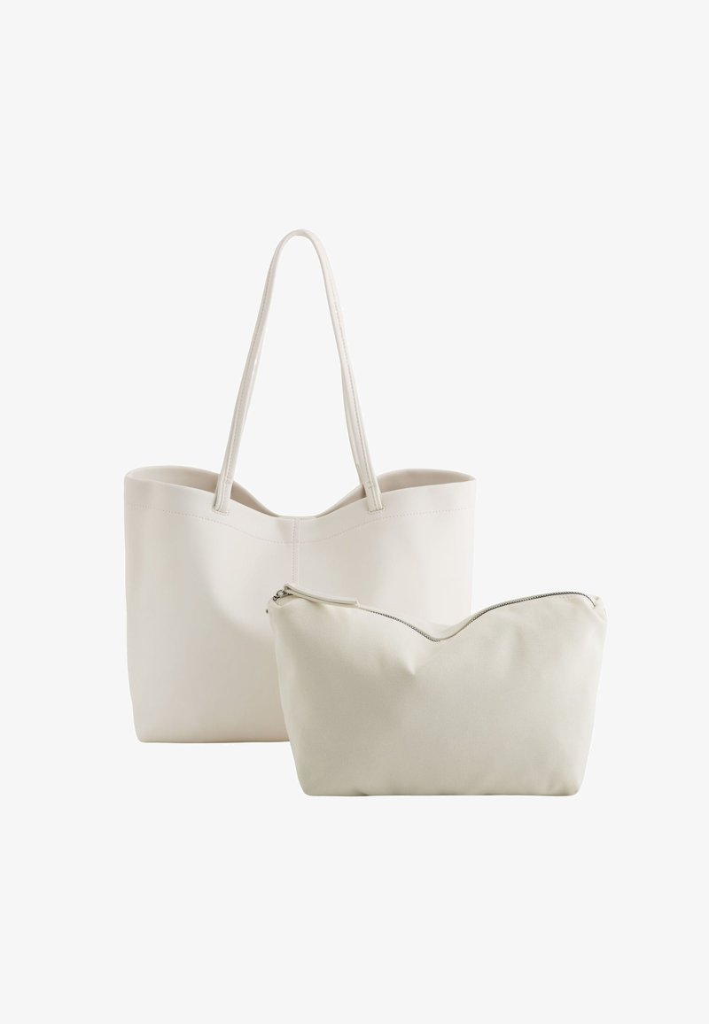 Bolso tote blanco con asas largas y material suave, acompañado de un pouch blanco más pequeño con cierre de cremallera y borde superior curvado.