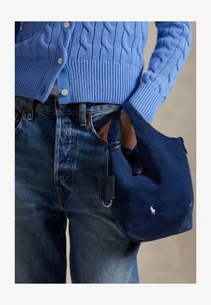 Tamnoplava kožna torba od brušene kože s mekanom teksturom, dvostrukim ručkama i malom privjeskom. Na prednjoj strani nalazi se bijeli logo i zaobljeno dno.