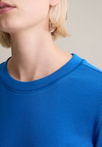 Geripptes, blaues Baumwoll-T-Shirt mit rundem Ausschnitt, glatter Textur und sichtbaren Nähtelementen am Kragen und an den Ärmeln.