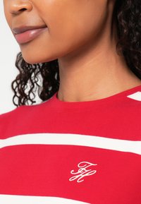 Red striped top features wide white stripes with an embroidered logo on the chest. The fabric appears smooth and stretchy.