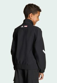 Zwarte jas met hoge kraag, elastische manchetten en zoom. Voorzien van witte accenten en logo's op de achterkant. Gemaakt van een lichtgewicht materiaal.