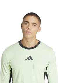 lichtgroen langemouwen shirt met zwarte accenten, met twee borstzakken en een ronde halslijn. Adidas-logo in het zwart op de voorkant.
