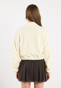 Light yellow soft fabric sweatshirt with gathered hem, paired with a dark pleated mini skirt featuring frayed edges.