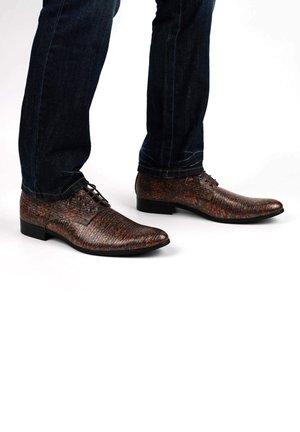 Chaussures habillées multicolores à texture, dotées d'un bout pointu, d'un talon plat et d'un design à lacets, associées à un jean en denim bleu foncé.