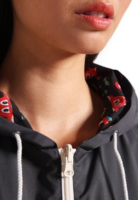 Ciemnoszara kurtka z kapturem z kontrastowym, kolorowym, wzorzystym wnętrzem. Zamek błyskawiczny z przodu oraz białe sznurki.