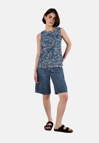 Top senza maniche blu con un motivo a foglie, abbinato a pantaloni shorts di jeans a ginocchio. Sandali neri completano l'outfit.